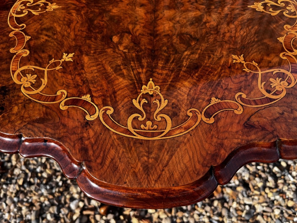 A Victorian burr walnut wine table featuring a scalloped top with floral marquetry inlay, a carved central pedestal, and tripod legs. View VIII