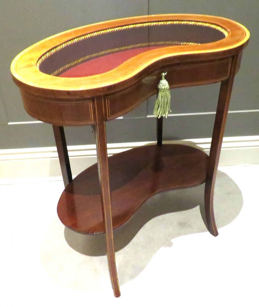 An Edwardian kidney-shaped mahogany bijouterie table featuring fine satinwood inlay, a glass-topped display section lined in burgundy fabric, and a lower shelf. View II
