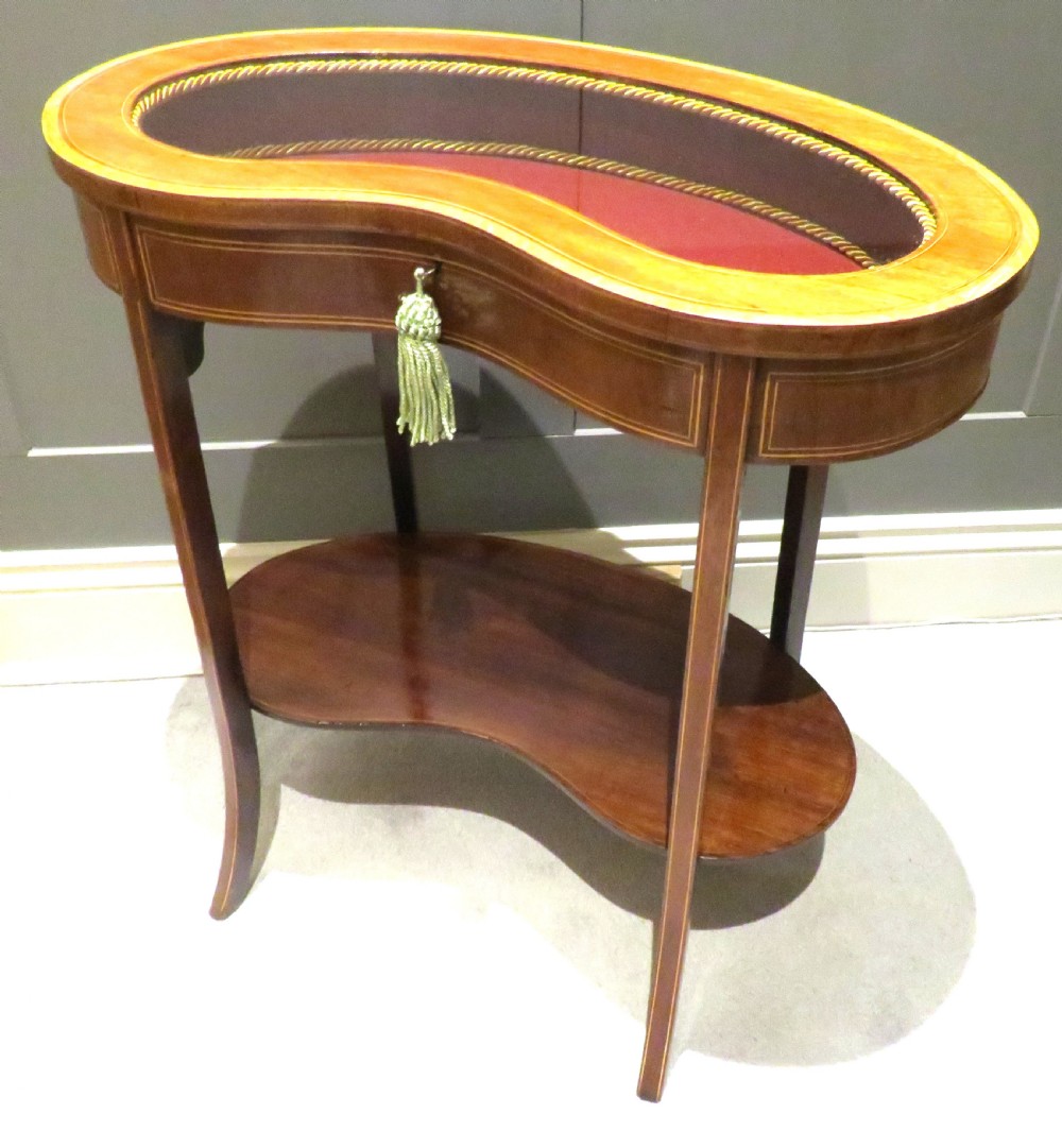 An Edwardian kidney-shaped mahogany bijouterie table featuring fine satinwood inlay, a glass-topped display section lined in burgundy fabric, and a lower shelf. View III