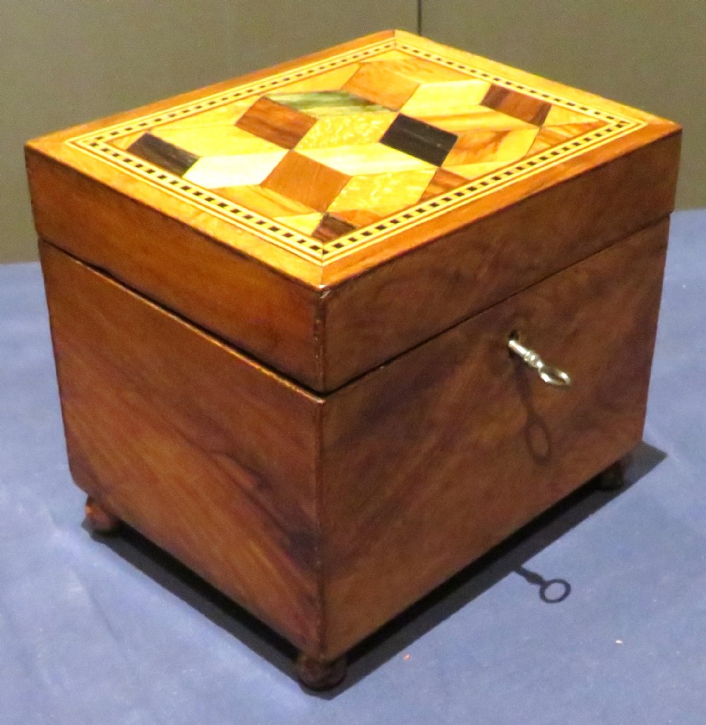 A rectangular wooden tea caddy featuring a geometric tumbling blocks parquetry inlay on the lid, small feet, and a key in the keyhole.