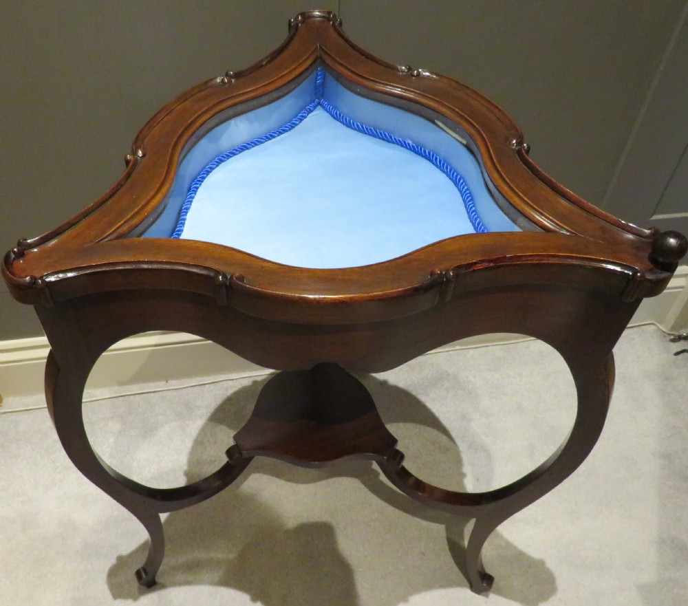 An Edwardian clover-shaped mahogany bijouterie table featuring a hinged glazed top, blue fabric lining, lower shelf, and cabriole legs. View V