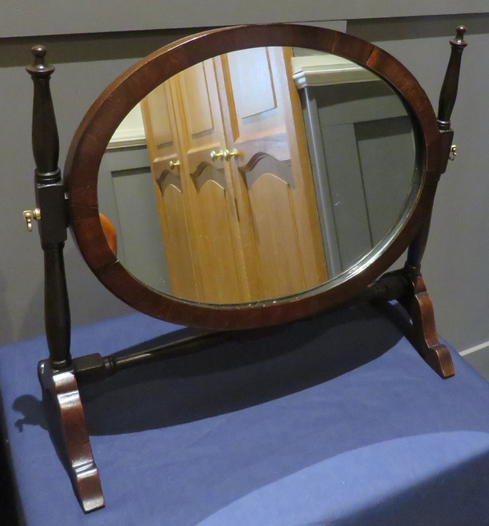 Victorian mahogany swing mirror featuring an oval frame held between two turned upright posts on trestle feet.