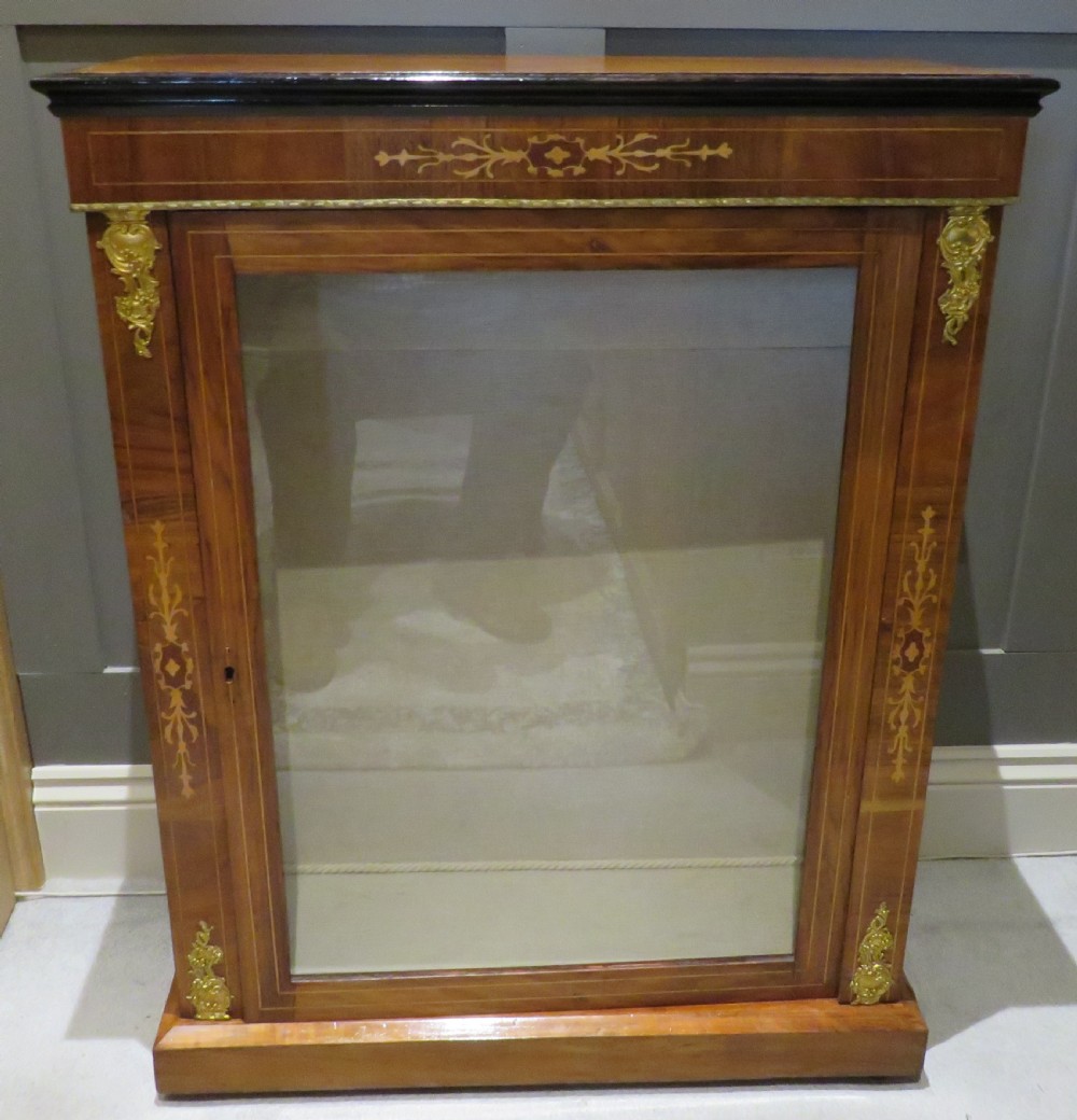 A Victorian walnut pier cabinet featuring a single glazed door, floral marquetry inlay, and gilt brass corner mounts.