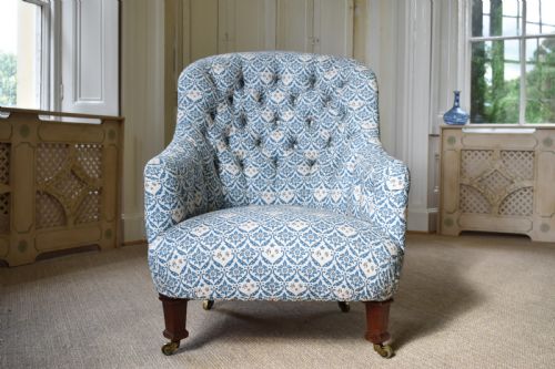 fig 1. A deep Victorian button-back armchair upholstered in patterned blue and white fabric, set on turned mahogany front legs with brass castors.