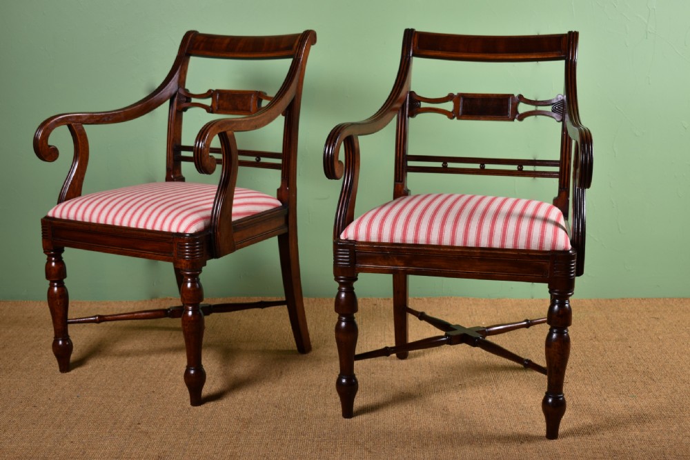 A pair of antique Scottish Regency mahogany armchairs featuring scrolled arms, turned front legs, and pink striped fabric seat cushions.