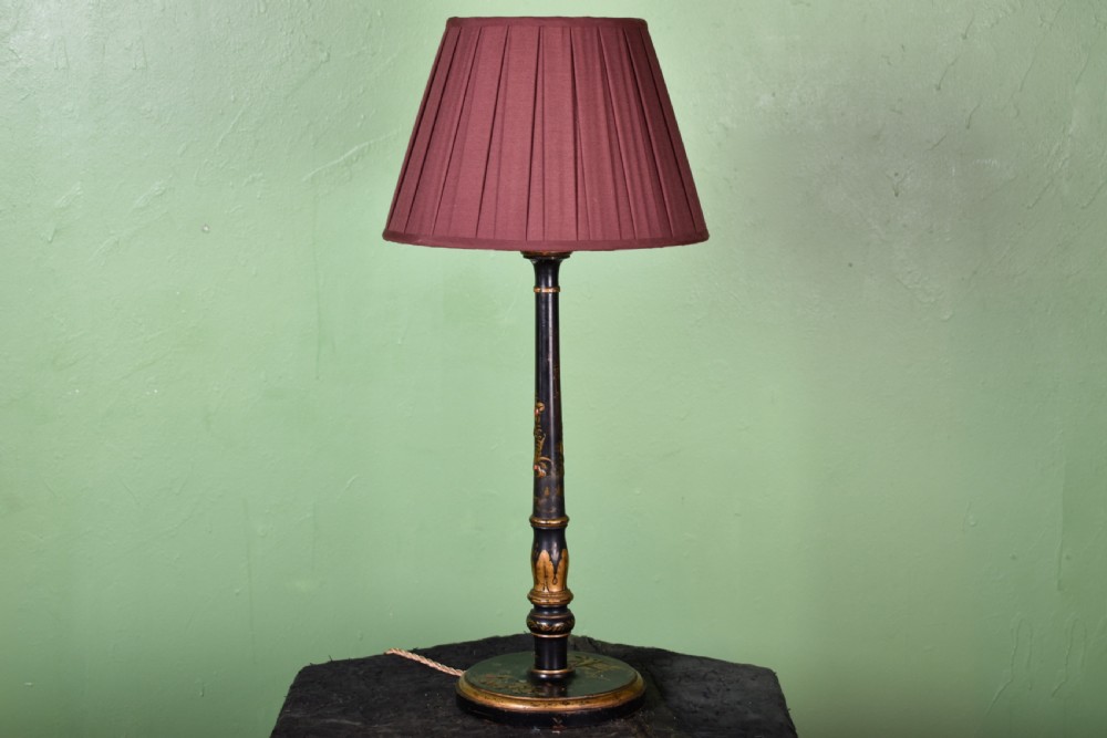 A black lacquered turned column table lamp with hand-painted gilt Chinoiserie decoration and a pleated burgundy fabric shade.