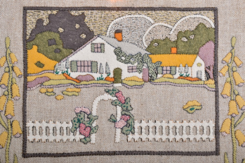 A framed textile needlework picture featuring a stitched country cottage landscape, a four-line poem, foxgloves, bleeding hearts, a cat, and a dog on a natural linen ground. View II