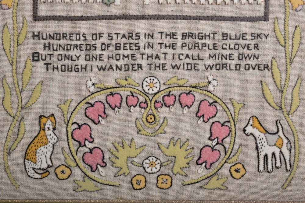 A framed textile needlework picture featuring a stitched country cottage landscape, a four-line poem, foxgloves, bleeding hearts, a cat, and a dog on a natural linen ground. View III