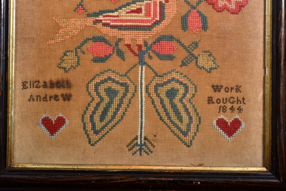An 1844 Victorian needlework sampler framed in dark wood featuring a central bird, red flowers, two hearts, and hand-stitched lettering. View III