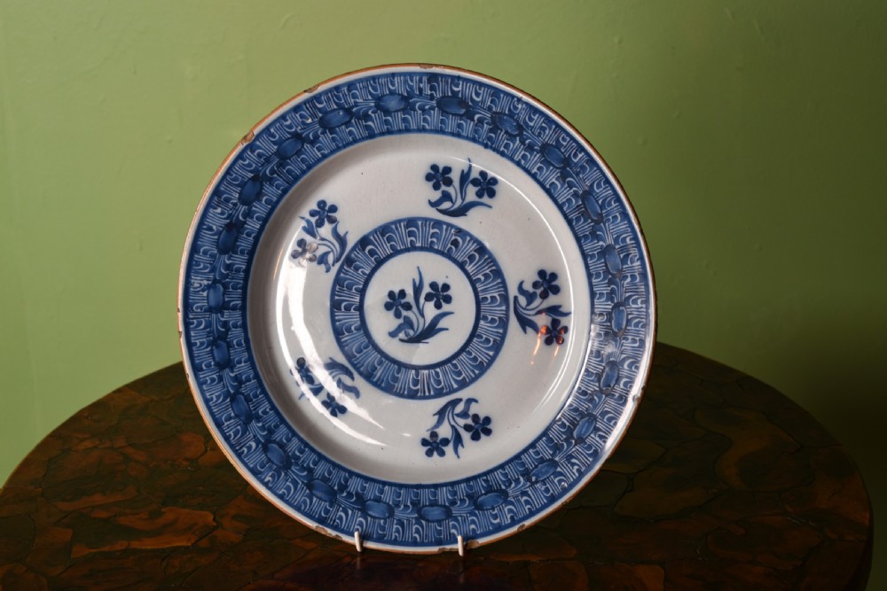 A circular antique blue and white tin-glazed earthenware shallow bowl decorated with hand-painted floral sprigs and concentric patterned borders.