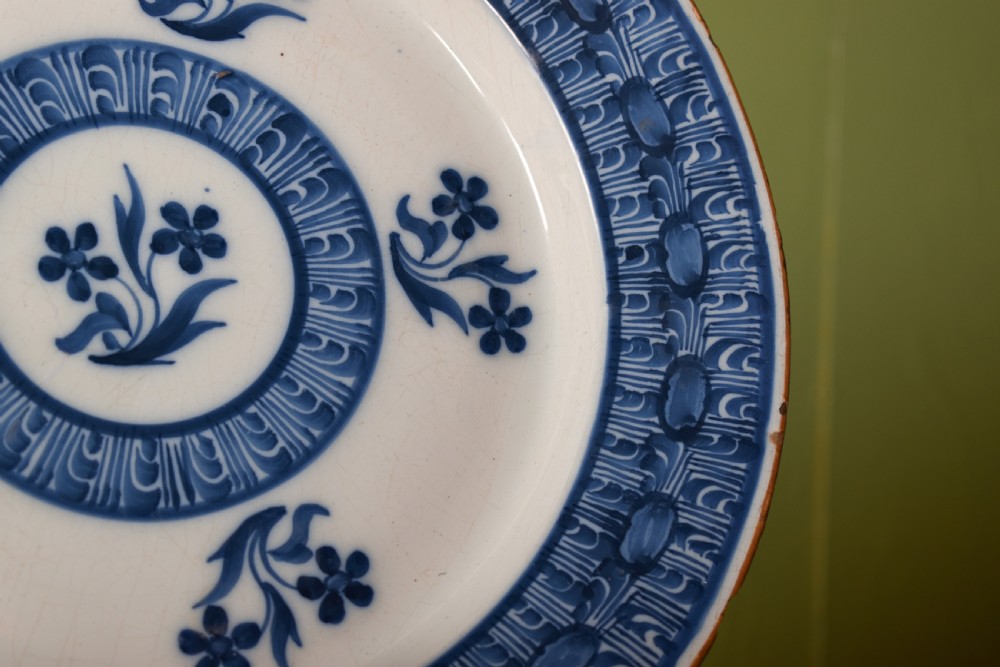 A circular antique blue and white tin-glazed earthenware shallow bowl decorated with hand-painted floral sprigs and concentric patterned borders. View III