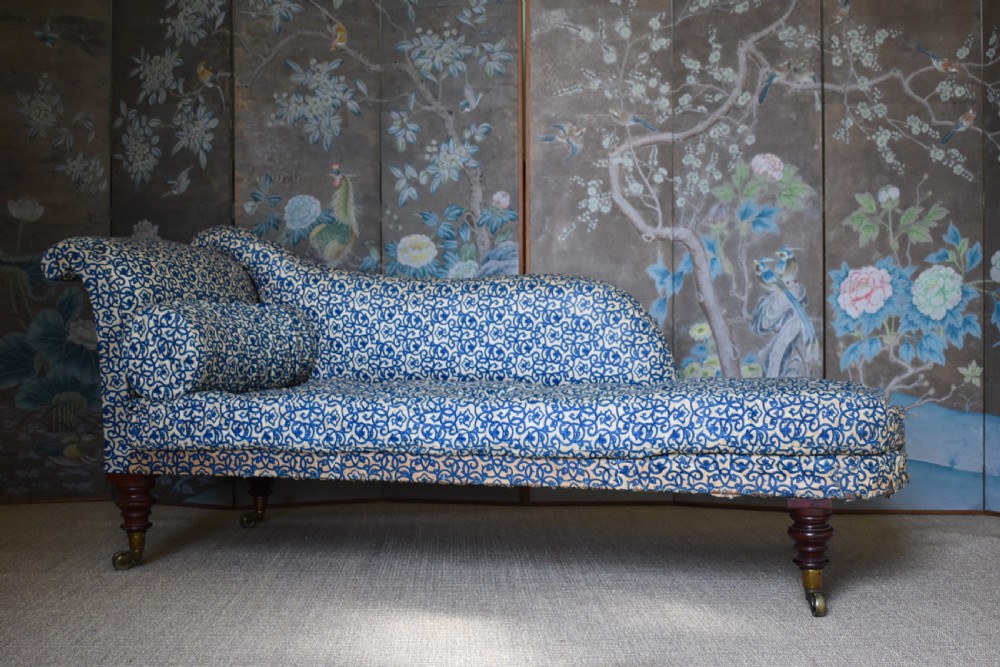 A Victorian upholstered chaise longue featuring a blue and white patterned fabric, a matching bolster cushion, and turned dark wood legs on brass castors.