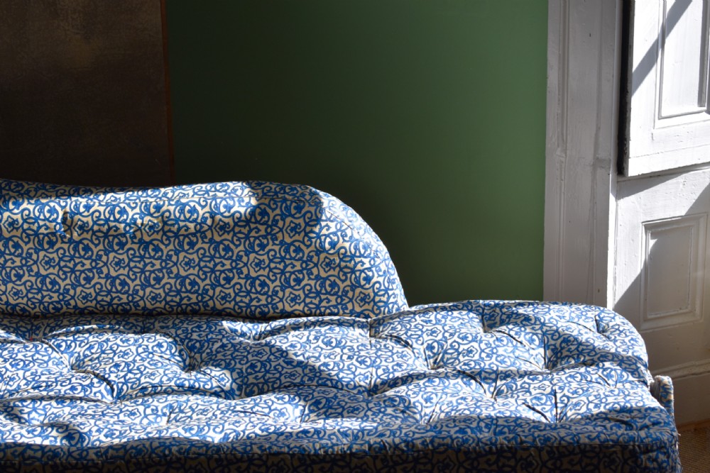 A Victorian upholstered chaise longue featuring a blue and white patterned fabric, a matching bolster cushion, and turned dark wood legs on brass castors. View II