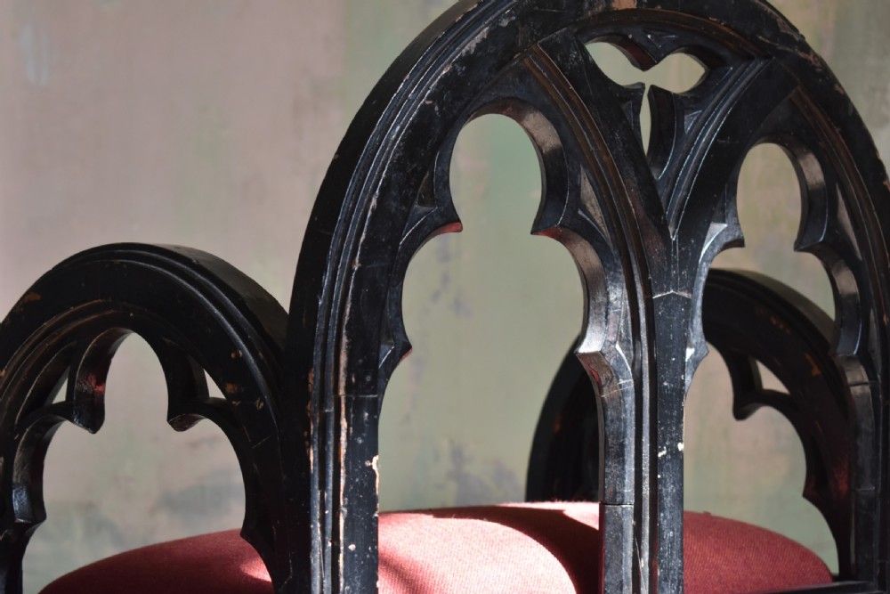 A pair of distressed black painted Gothic Revival armchairs featuring carved lancet tracery cutouts and red upholstered seats. View V
