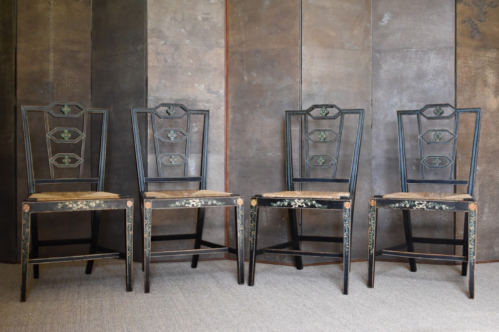 A set of four George III black-painted side chairs featuring geometric lattice backs with painted medallions, floral apron details, and woven rush seats.