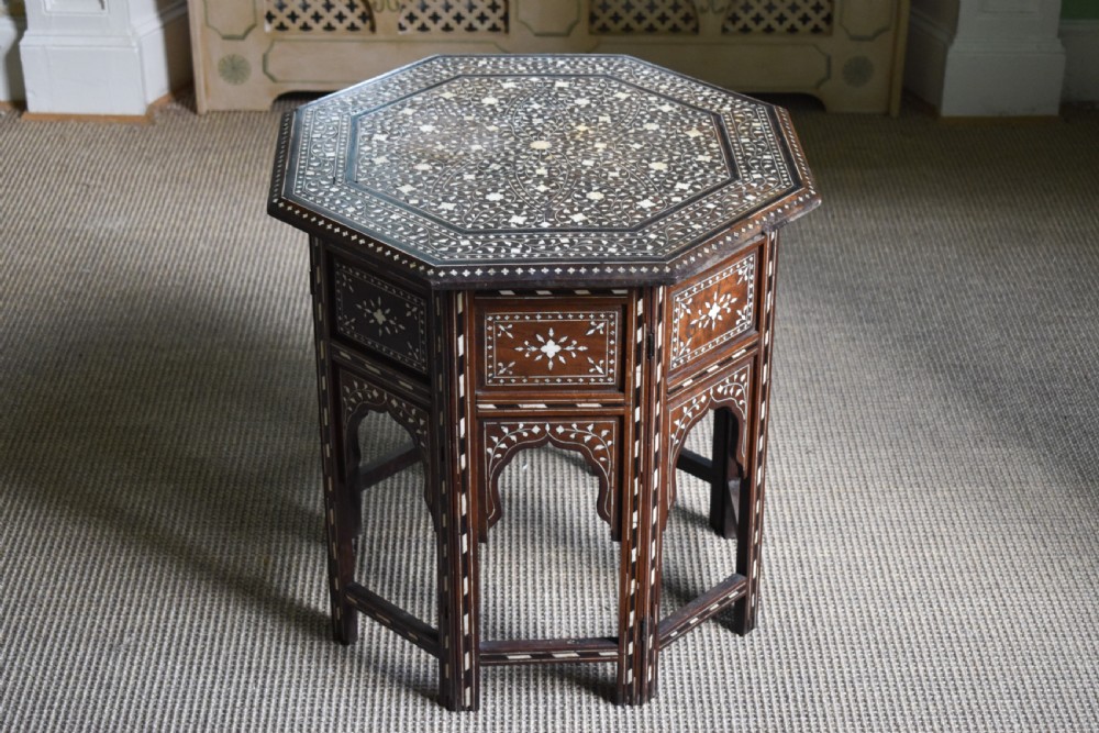 An octagonal dark wood side table featuring intricate bone inlay floral pattern work and decorative arched aprons.