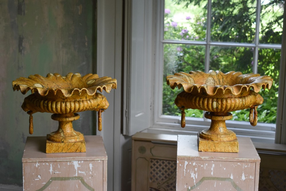 A pair of yellow painted cast iron urns with scalloped rims, gadrooned bodies, and square pedestal bases.