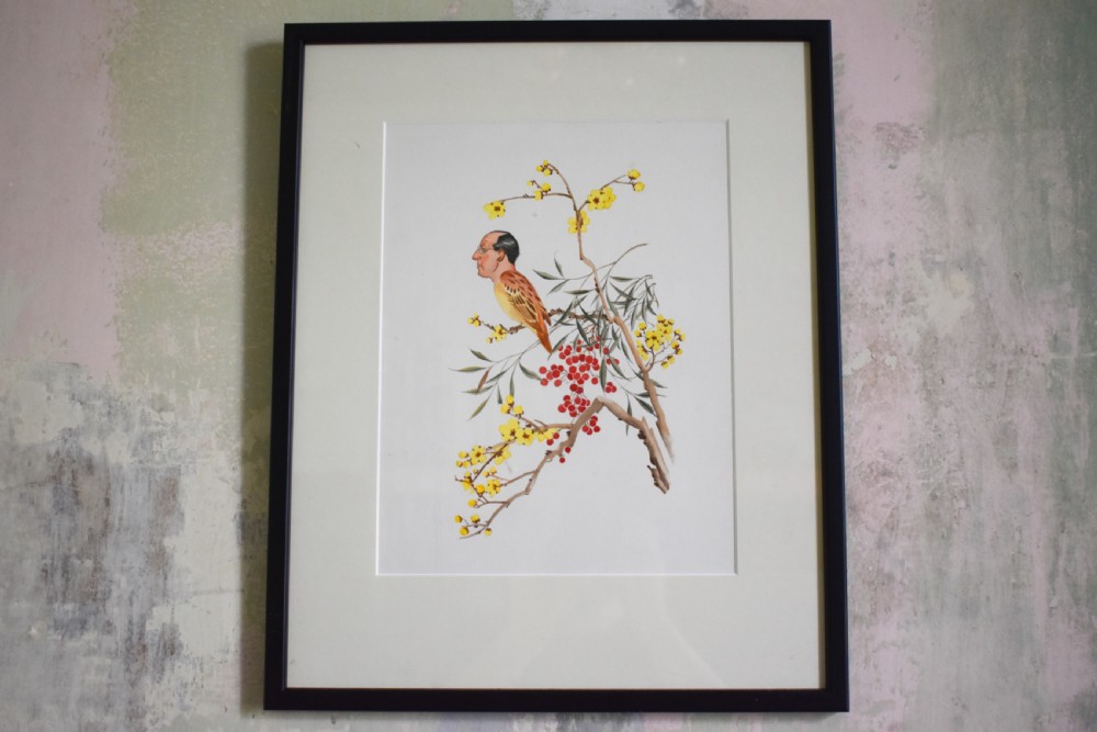 A framed watercolour artwork featuring a bird with a mans face perched on a botanical branch with yellow flowers and red berries, set within a cream mount and black frame.