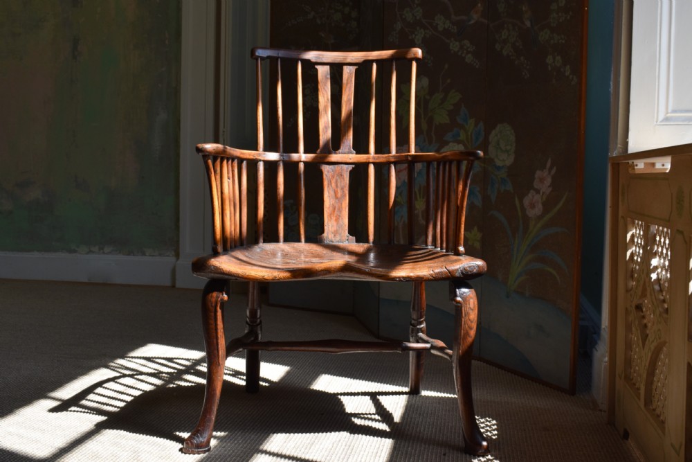 A George III wooden Windsor armchair featuring a shaped saddle seat, comb back rest with splat, and cabriole front legs.