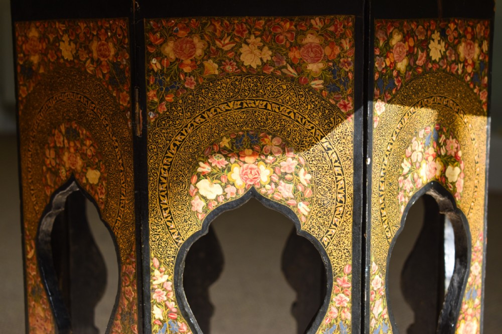 An octagonal Indian Kashmiri side table featuring intricate hand-painted floral motifs in gold, red, and green on a dark lacquered ground, resting alongside its matching folding arch-shaped base. View II