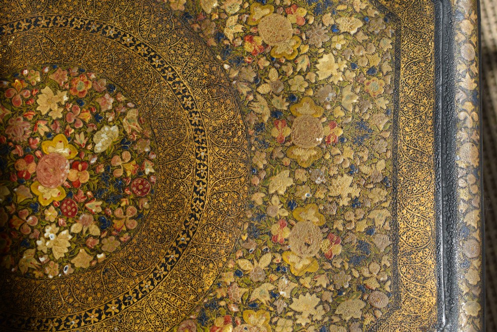 An octagonal Indian Kashmiri side table featuring intricate hand-painted floral motifs in gold, red, and green on a dark lacquered ground, resting alongside its matching folding arch-shaped base. View III