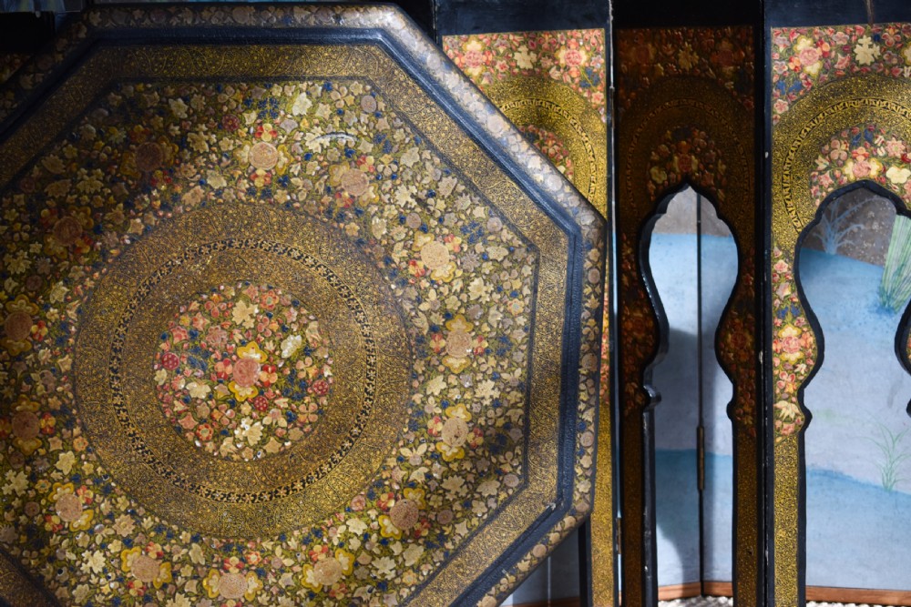 An octagonal Indian Kashmiri side table featuring intricate hand-painted floral motifs in gold, red, and green on a dark lacquered ground, resting alongside its matching folding arch-shaped base. View V