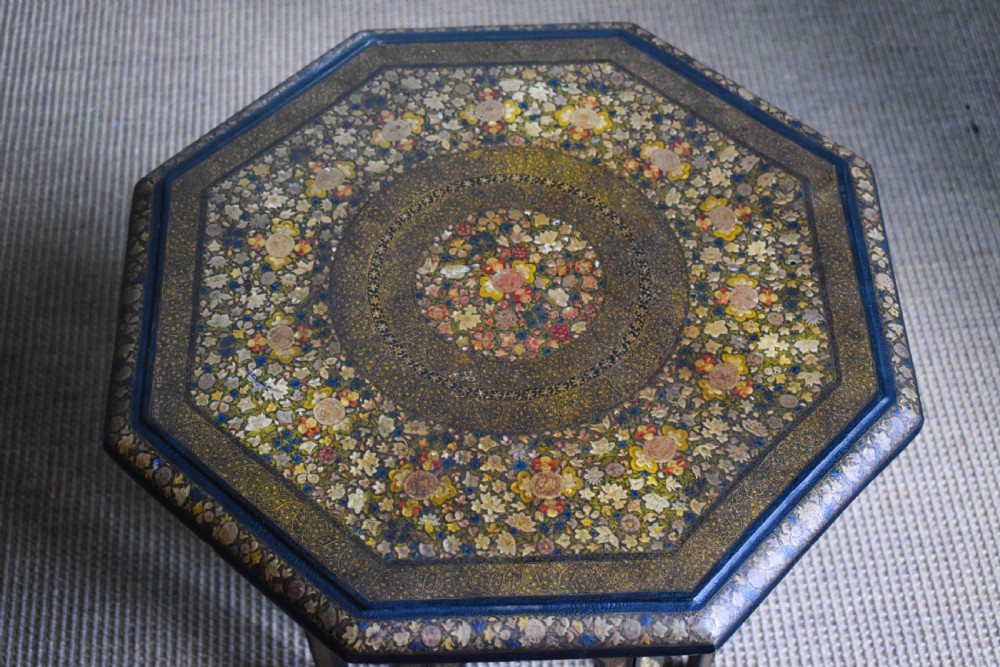 An octagonal Indian Kashmiri side table featuring intricate hand-painted floral motifs in gold, red, and green on a dark lacquered ground, resting alongside its matching folding arch-shaped base. View VI