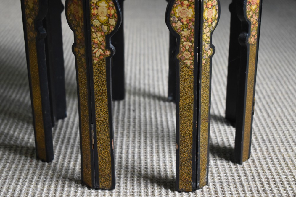 An octagonal Indian Kashmiri side table featuring intricate hand-painted floral motifs in gold, red, and green on a dark lacquered ground, resting alongside its matching folding arch-shaped base. View VII