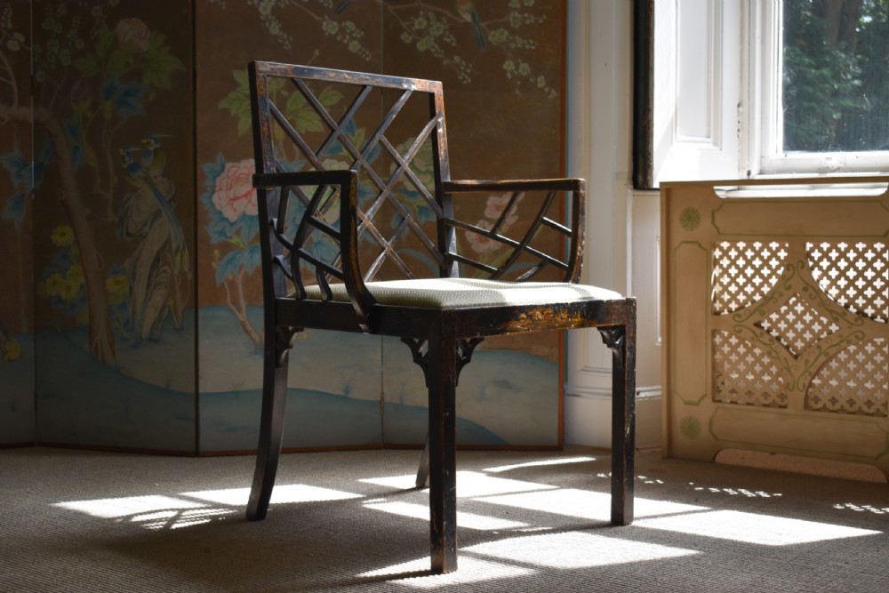 An antique ebonised Chinoiserie Cockpen armchair featuring a dark geometric lattice backrest, fretwork arm supports, straight legs, and a light-coloured fabric seat.