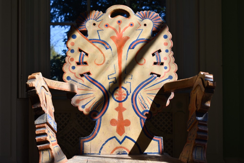 A Swedish folk art wooden armchair with a carved backrest featuring yellow, red, and blue painted details. View II