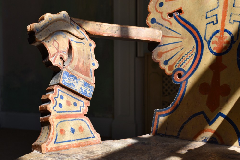 A Swedish folk art wooden armchair with a carved backrest featuring yellow, red, and blue painted details. View IV
