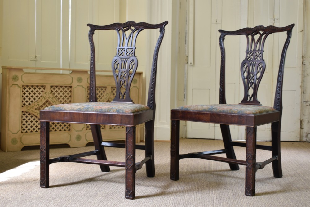 A pair of dark mahogany side chairs with intricate pierced back splats, carved square legs with fretwork, and tapestry fabric seats.