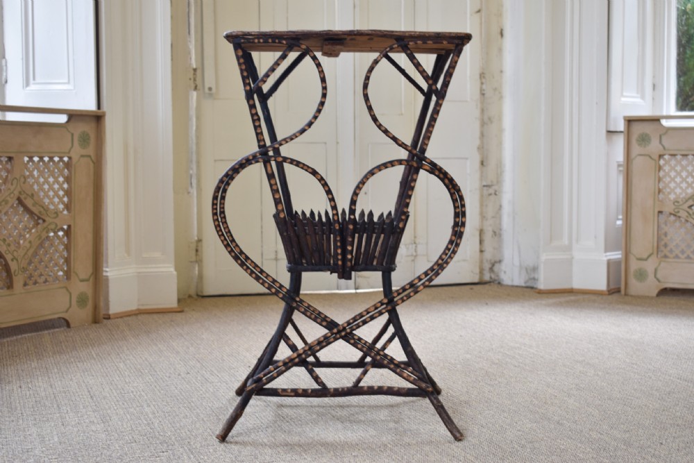 An antique folk art side table crafted from dark bent twigs with decorative notched patterns and arched bracing.
