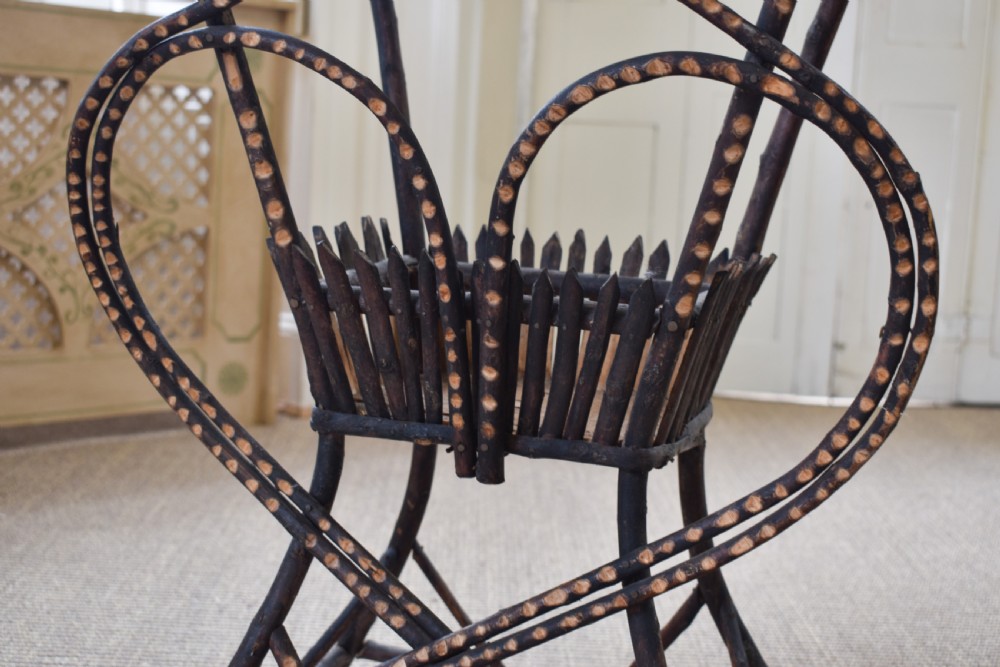 An antique folk art side table crafted from dark bent twigs with decorative notched patterns and arched bracing. View II