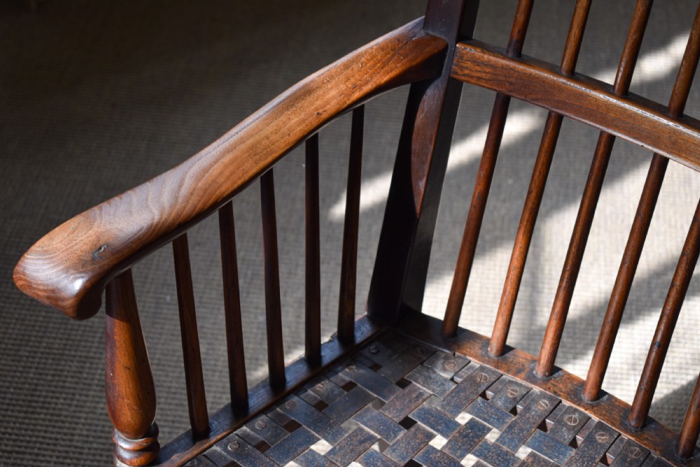 A dark timber country armchair featuring a tall spindle backrest, flat armrests on turned supports, a woven seat, and turned front legs. View III