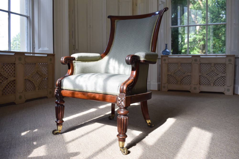 A George IV mahogany armchair with carved scroll arms, light green upholstery, and reeded turned front legs on brass castors.