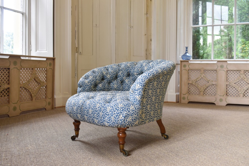 A deep-buttoned antique tub chair upholstered in a blue and white patterned fabric, set on turned timber legs with brass castors.