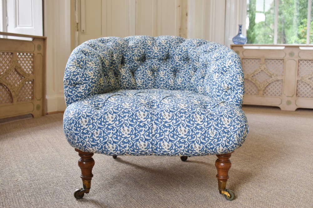 A deep-buttoned antique tub chair upholstered in a blue and white patterned fabric, set on turned timber legs with brass castors. View II