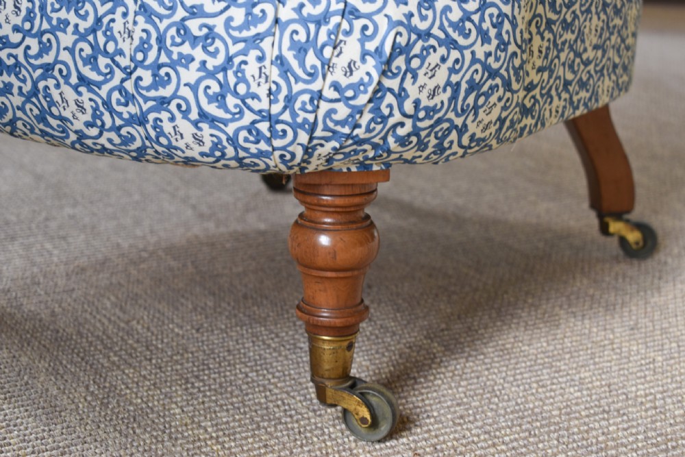 A deep-buttoned antique tub chair upholstered in a blue and white patterned fabric, set on turned timber legs with brass castors. View III