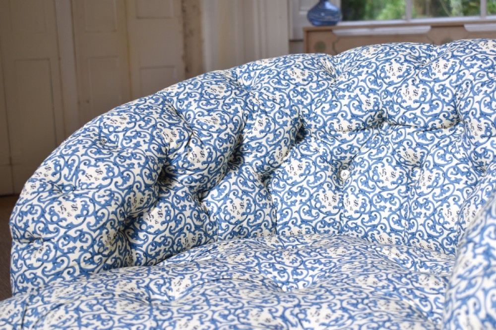 A deep-buttoned antique tub chair upholstered in a blue and white patterned fabric, set on turned timber legs with brass castors. View IV