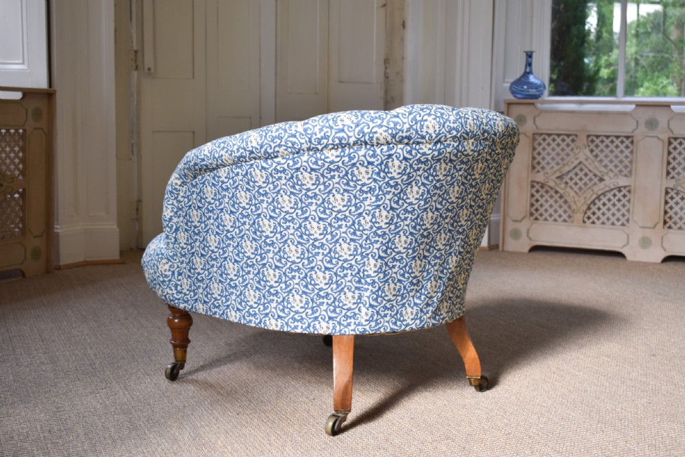 A deep-buttoned antique tub chair upholstered in a blue and white patterned fabric, set on turned timber legs with brass castors. View V