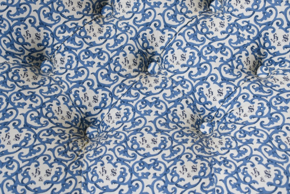 A low-seated Victorian slipper chair upholstered in blue and white patterned fabric with a button-tufted back and turned mahogany front legs on brass castors. View III
