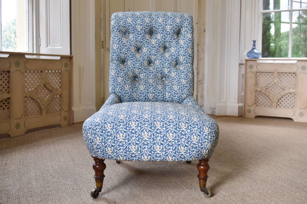 A low-seated Victorian slipper chair upholstered in blue and white patterned fabric with a button-tufted back and turned mahogany front legs on brass castors. View IV