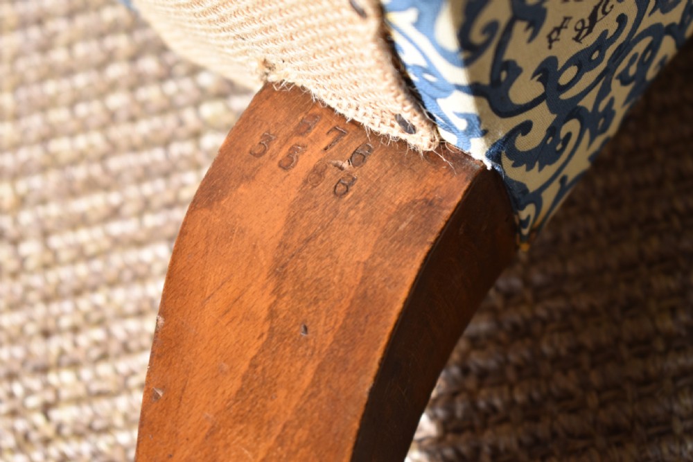 A low-seated Victorian slipper chair upholstered in blue and white patterned fabric with a button-tufted back and turned mahogany front legs on brass castors. View VI