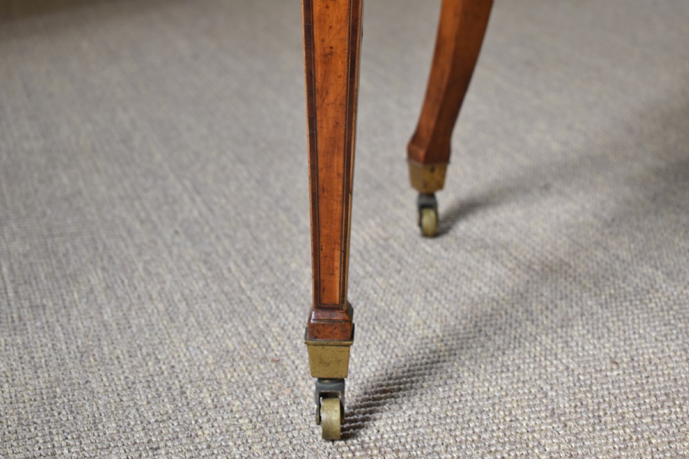 A George III satinwood open armchair featuring an oval upholstered backrest, light green fabric, padded armrests, and tapered legs on brass castors. View II