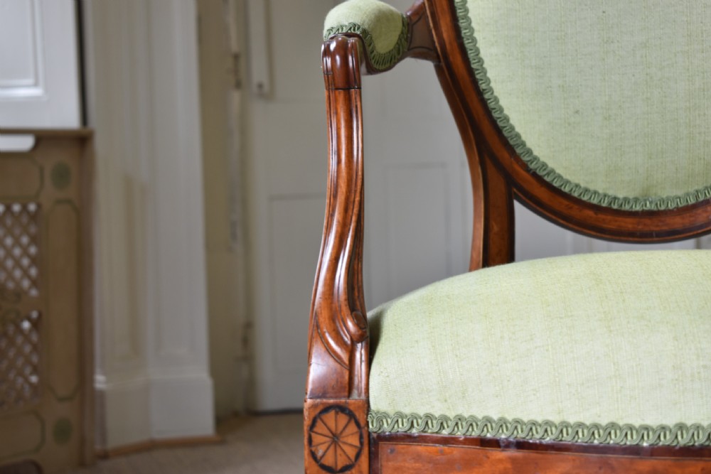 A George III satinwood open armchair featuring an oval upholstered backrest, light green fabric, padded armrests, and tapered legs on brass castors. View III