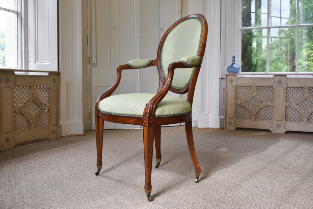 A George III satinwood open armchair featuring an oval upholstered backrest, light green fabric, padded armrests, and tapered legs on brass castors. View IV