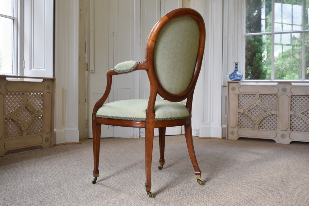 A George III satinwood open armchair featuring an oval upholstered backrest, light green fabric, padded armrests, and tapered legs on brass castors. View V