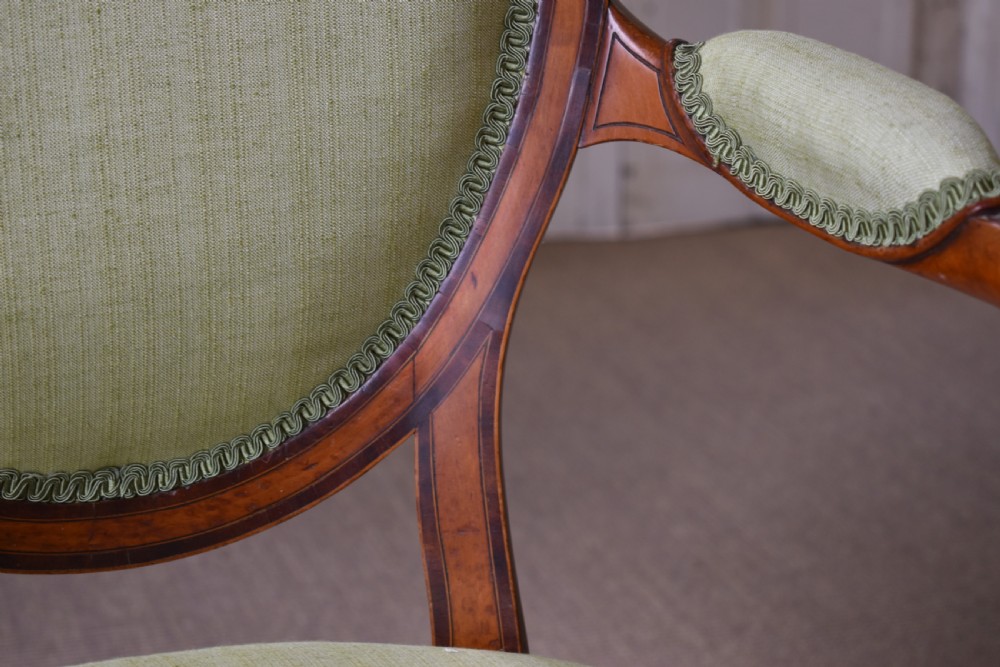 A George III satinwood open armchair featuring an oval upholstered backrest, light green fabric, padded armrests, and tapered legs on brass castors. View VI