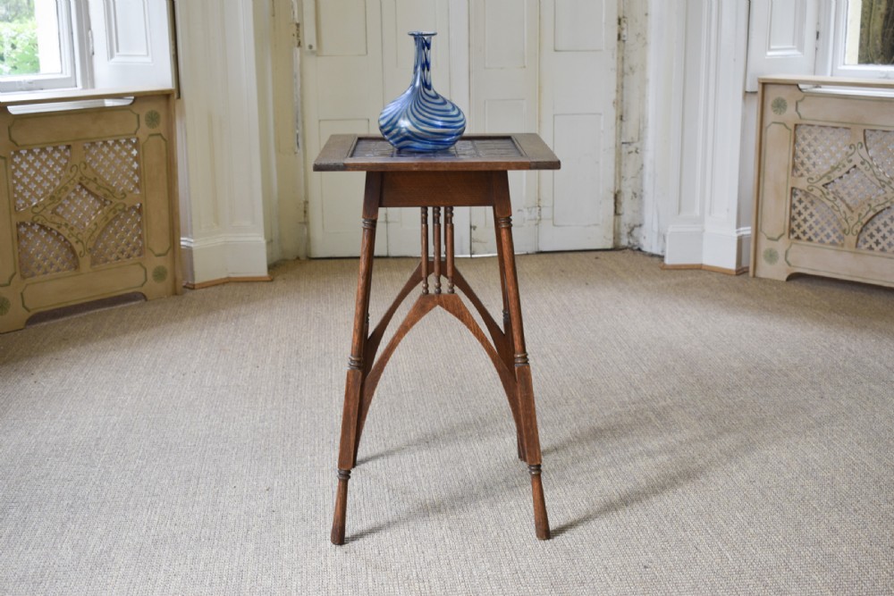 An antique Arts and Crafts oak occasional table featuring a square tiled inset top, arched bracing, and slender turned spindle legs. View II